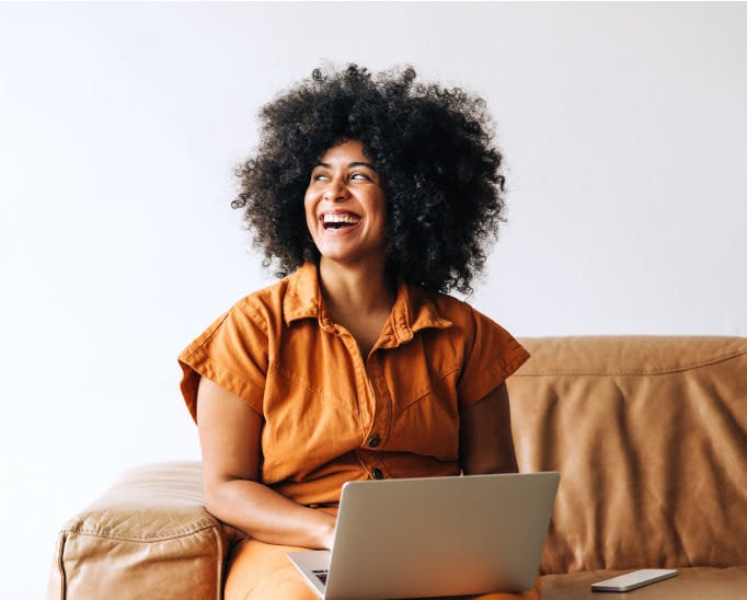 Woman smiling and sitting on a couch with a laptop