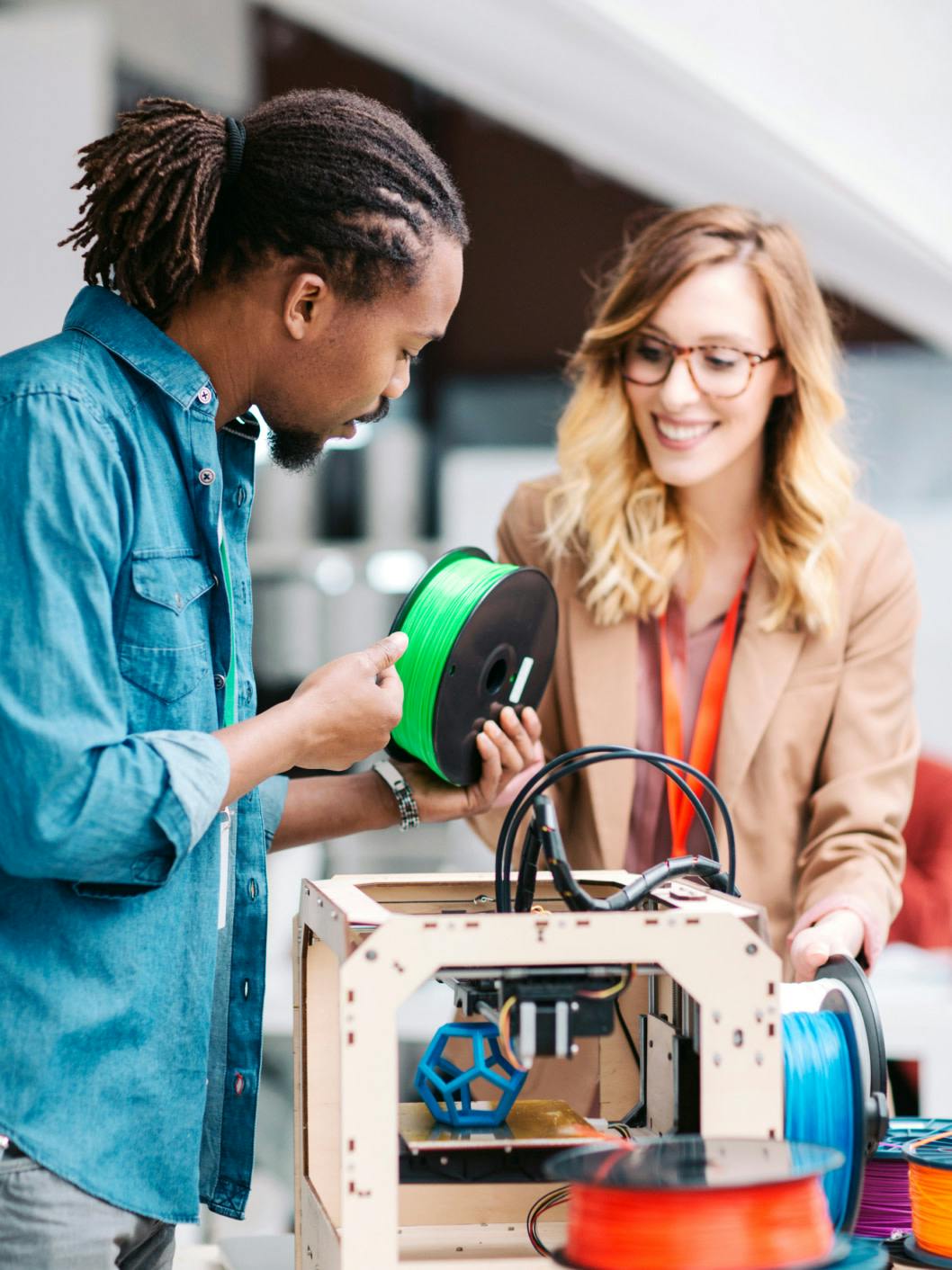 two people holding a spool next to a 3D printer